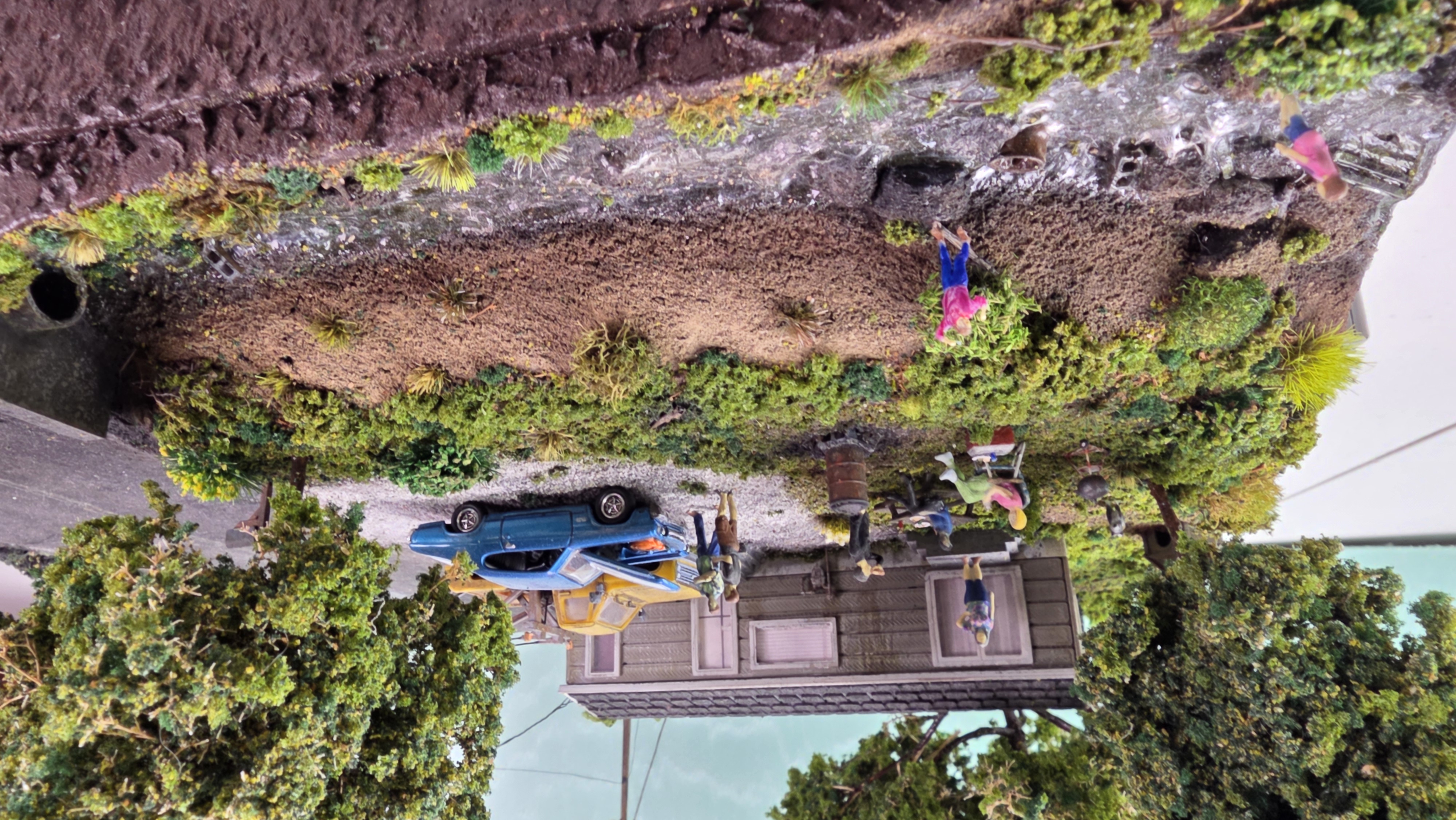 Kids playing in the HO scale creek running past the yard, with debris — a pallet, oil drum, cinder blocks, and tire — in the water