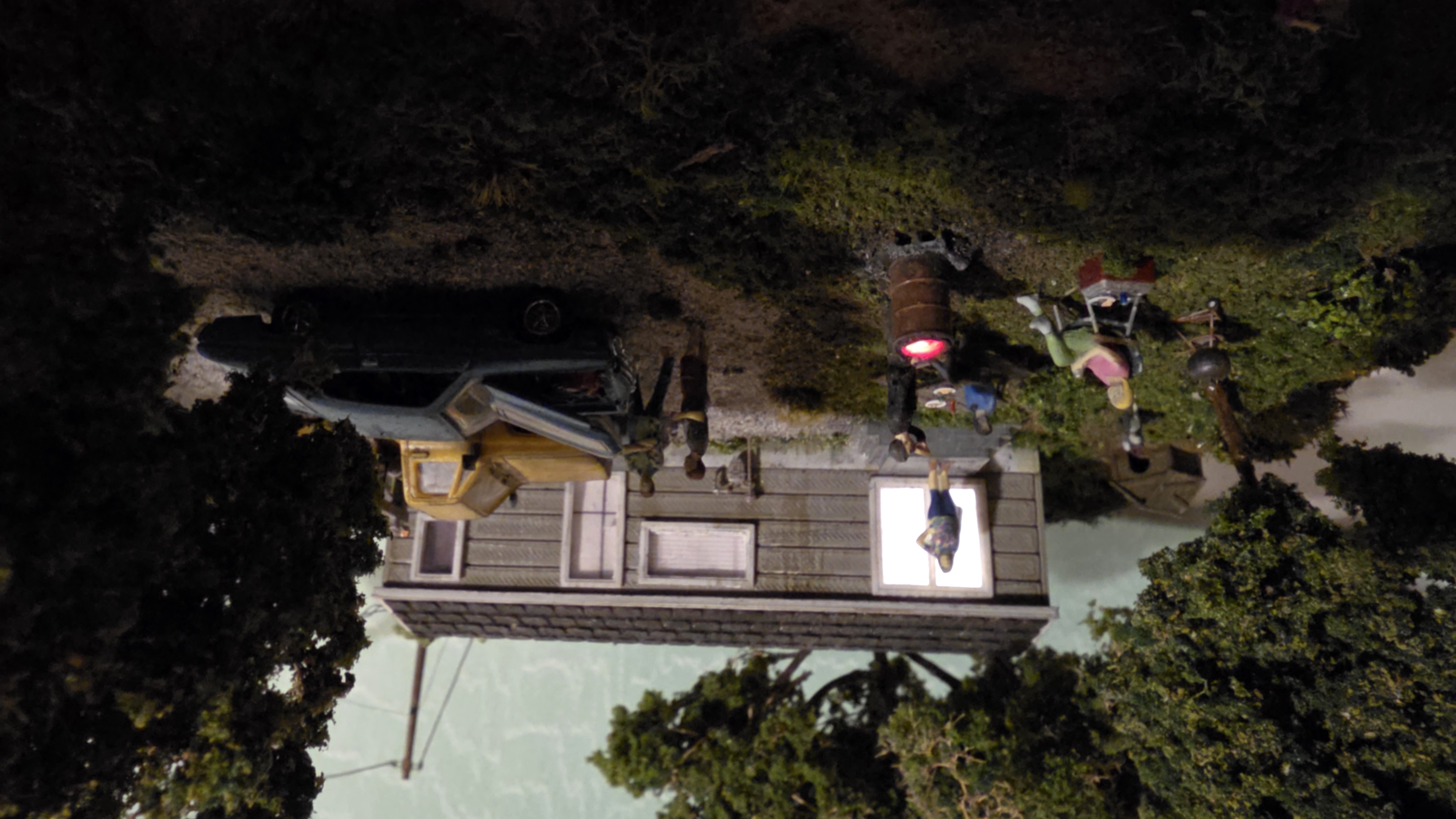 Night view of the HO scale cookout — the Arduino burn barrel glowing orange and the trailer's master-bedroom window lit